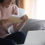 Smiling woman wearing glasses holding envelope with letter close up
