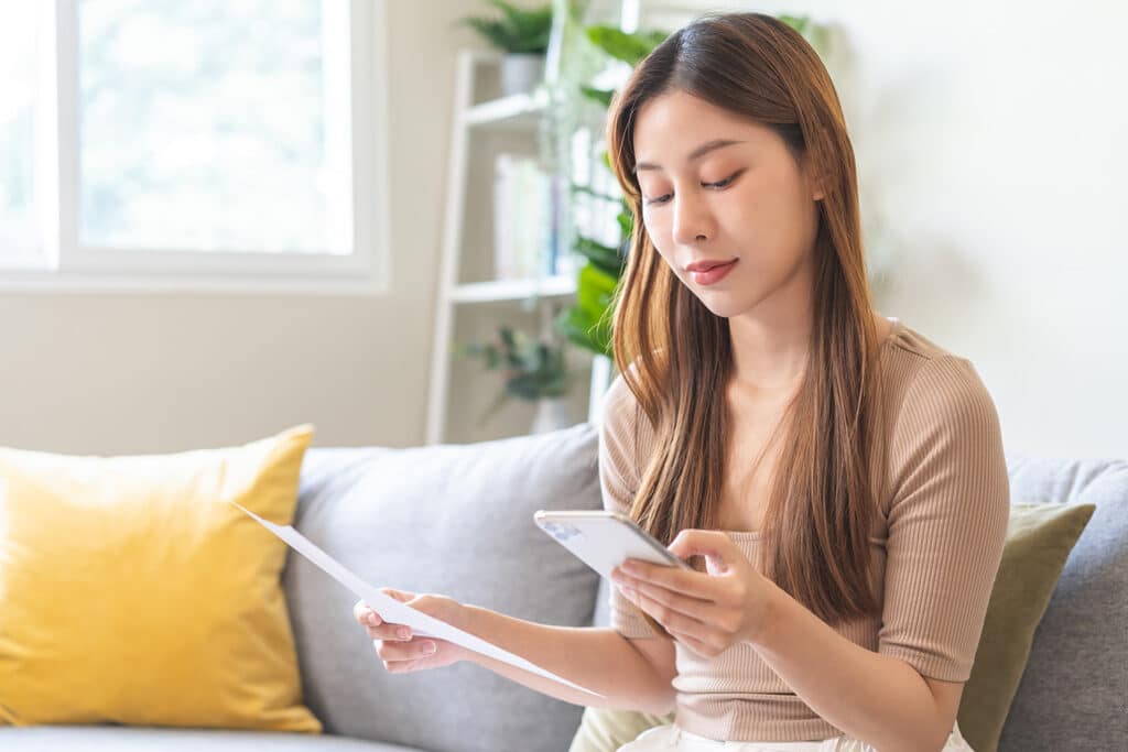 Smiling young woman calculate finances, hand holding mobile phone and invoice